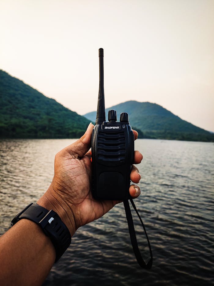 Services Close-up of a hand holding a walkie talkie with a lake and mountains in the background.