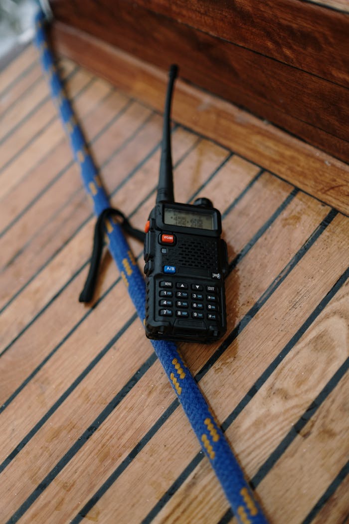 About A two-way radio placed on a wooden surface next to a blue rope, possibly on a boat deck.