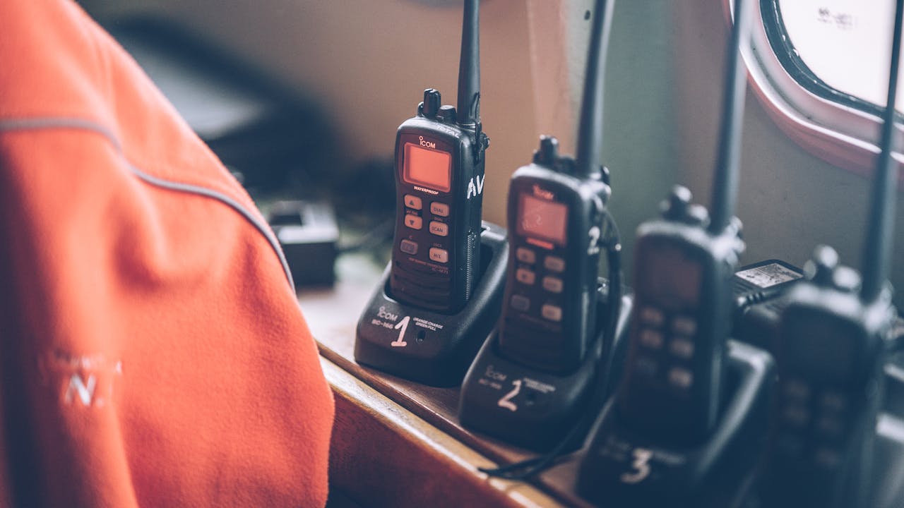 About Four wireless walkie talkies in charging stations on a wooden dock indoors.